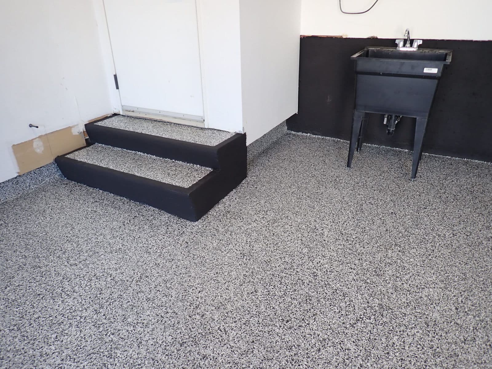 Intérieur de garage avec sol en époxy, marches d'accès à la porte, évier utilitaire, palette de couleurs noir et blanc.
