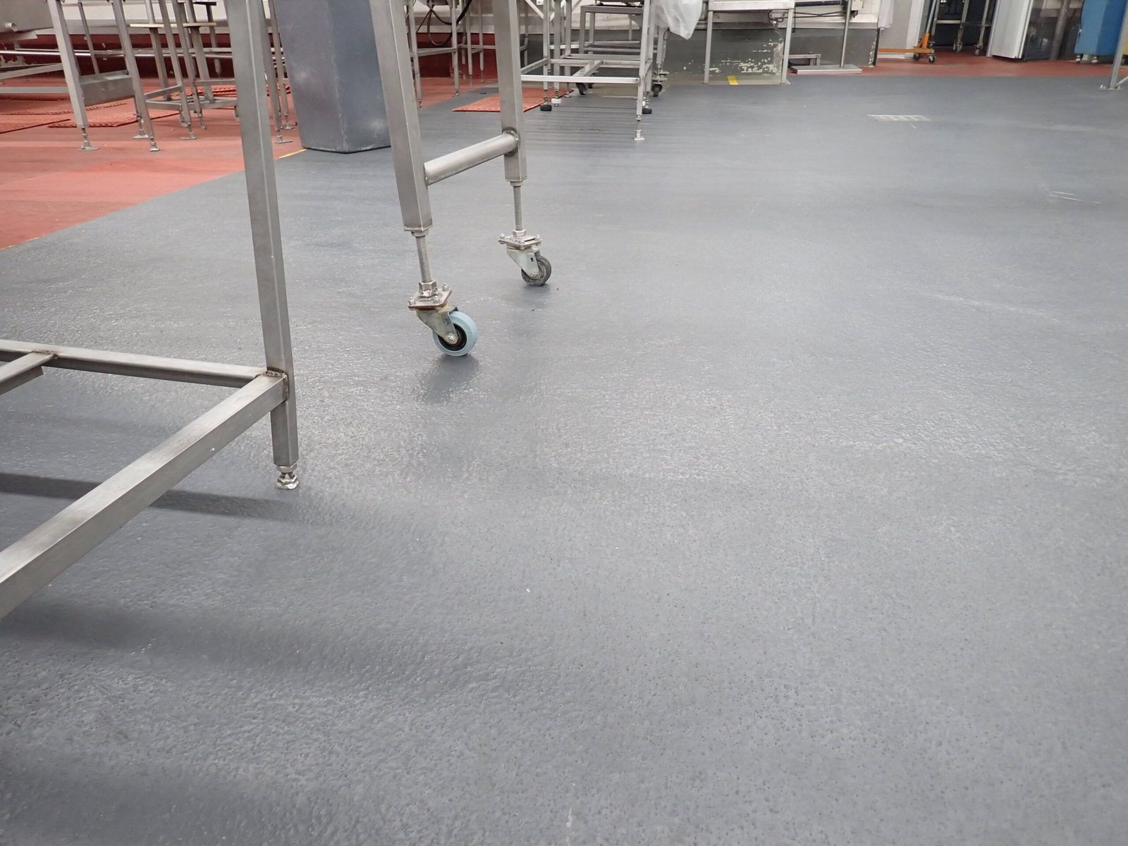 Sol industriel gris avec tables en acier inoxydable et bordure rouge.