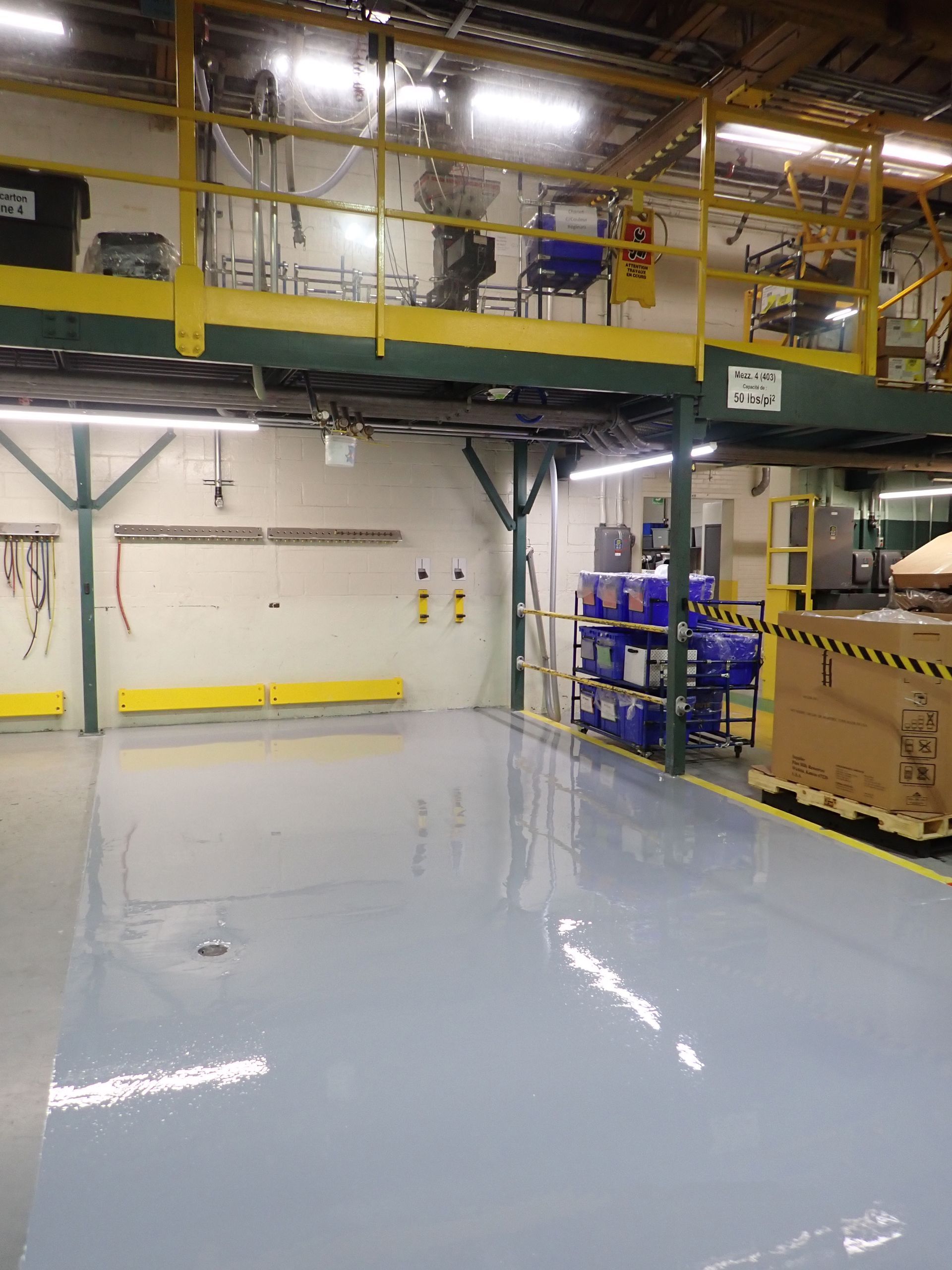 Intérieur de style industriel avec un sol gris, des barrières de sécurité jaunes et une plateforme surélevée à rambarde jaune.