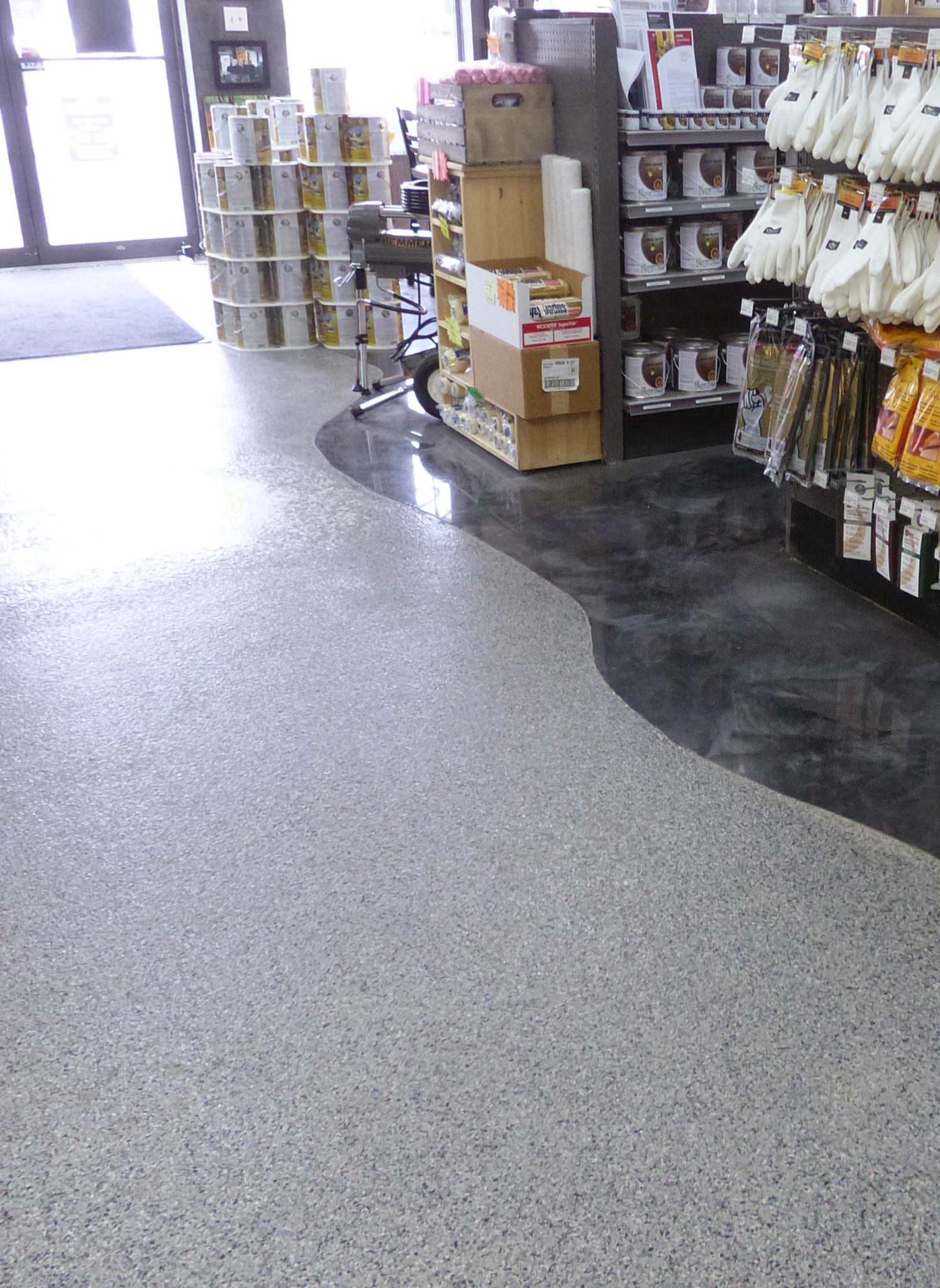 Sol en béton brillant et moucheté dans un magasin, avec une partie sombre et incurvée. Des étagères et des produits sont visibles.