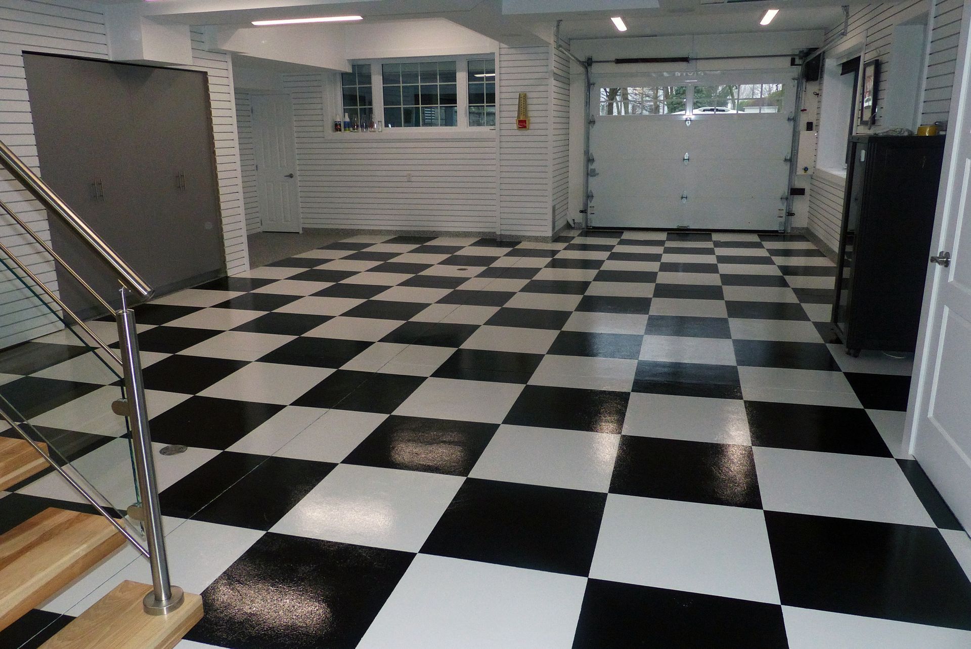 Un garage avec un sol à damier noir et blanc, des murs blancs et une porte de garage fermée.