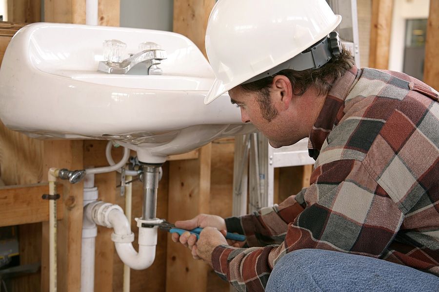 A man wearing a hard hat is fixing a sink with a wrench.