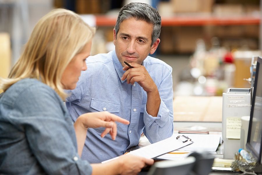 A man and a woman are sitting at a desk looking at a computer screen.