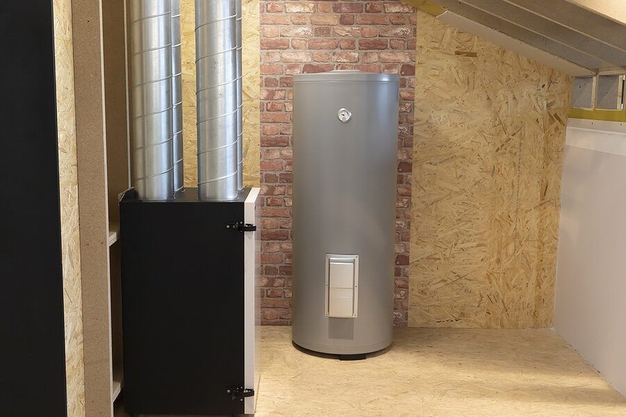 A water heater is sitting in a room next to a brick wall.