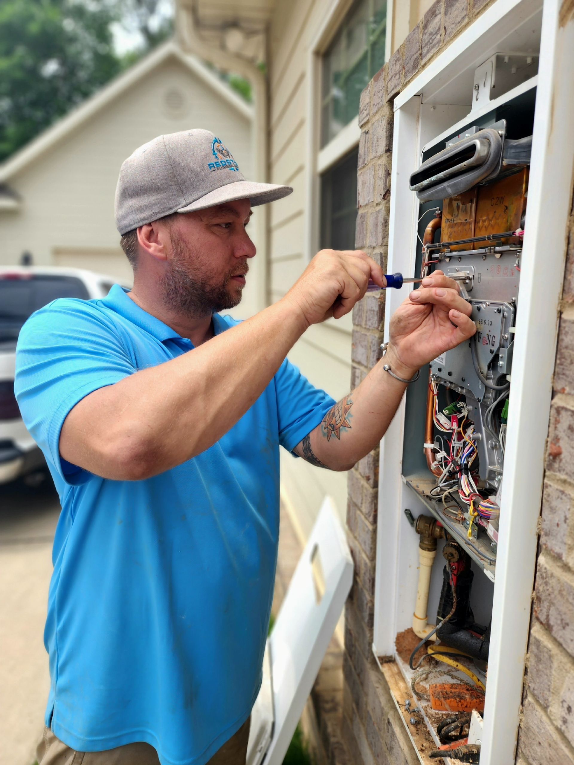 A man in a blue shirt is working on an air conditioner outside of a house.