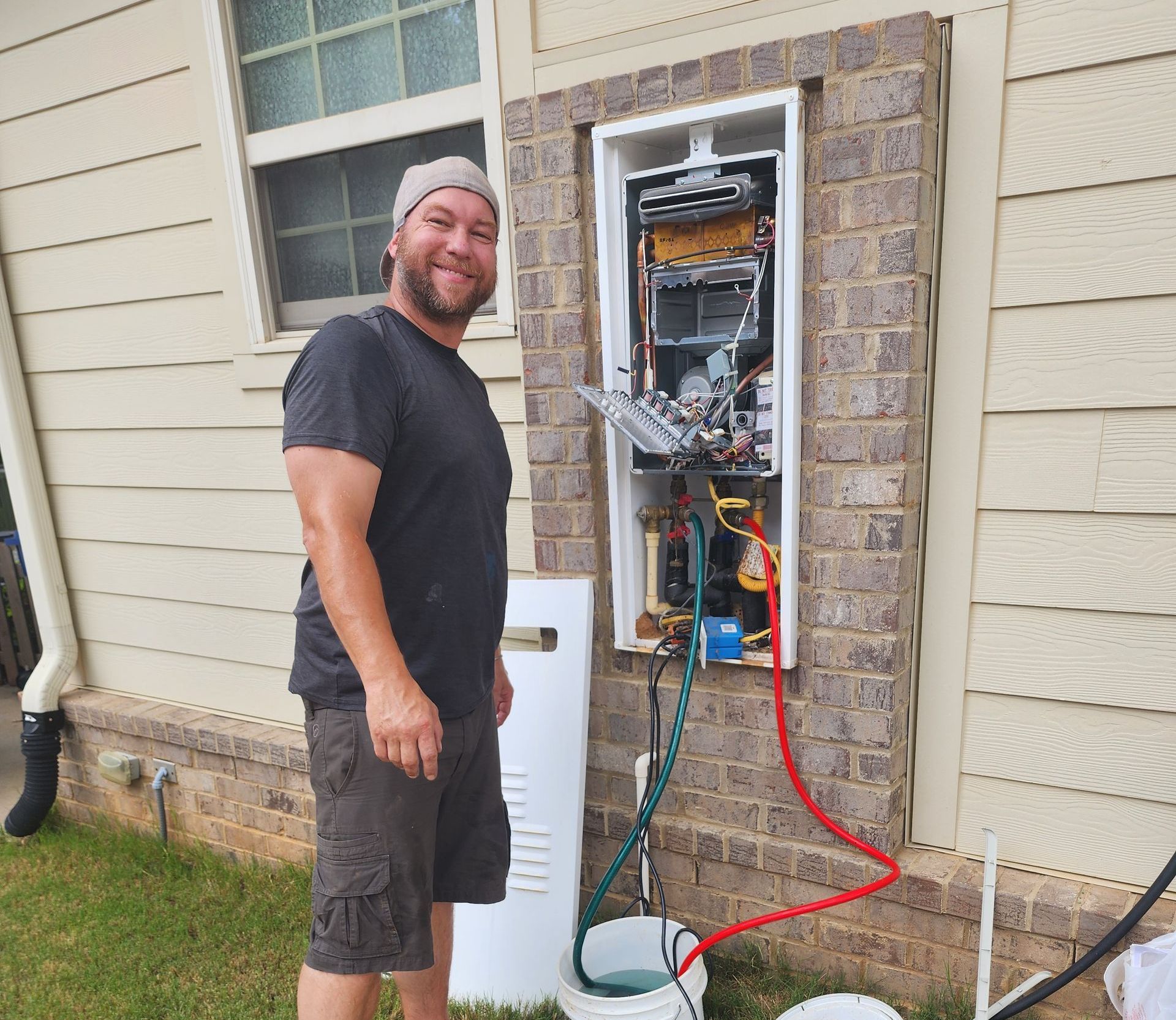 A man is standing in front of a boiler on the side of a house.