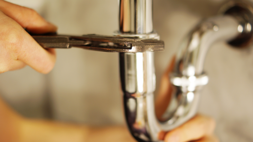 A person is fixing a pipe with a wrench.