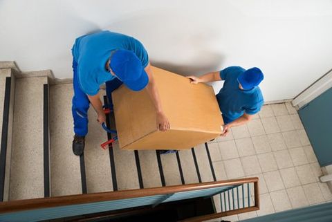 Two professionals carrying big box by stairs