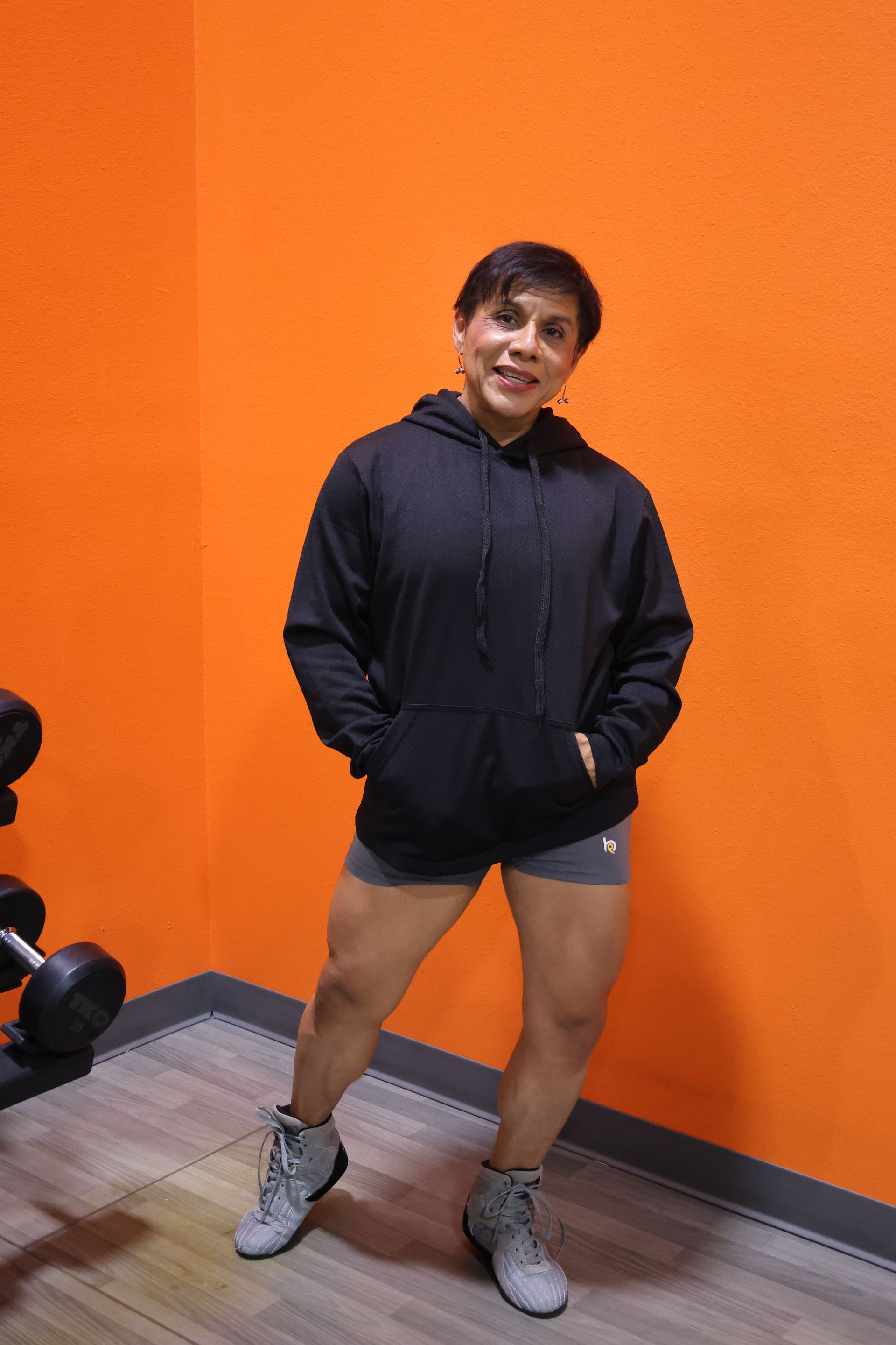 A woman in a black hoodie and shorts is standing in a gym.
