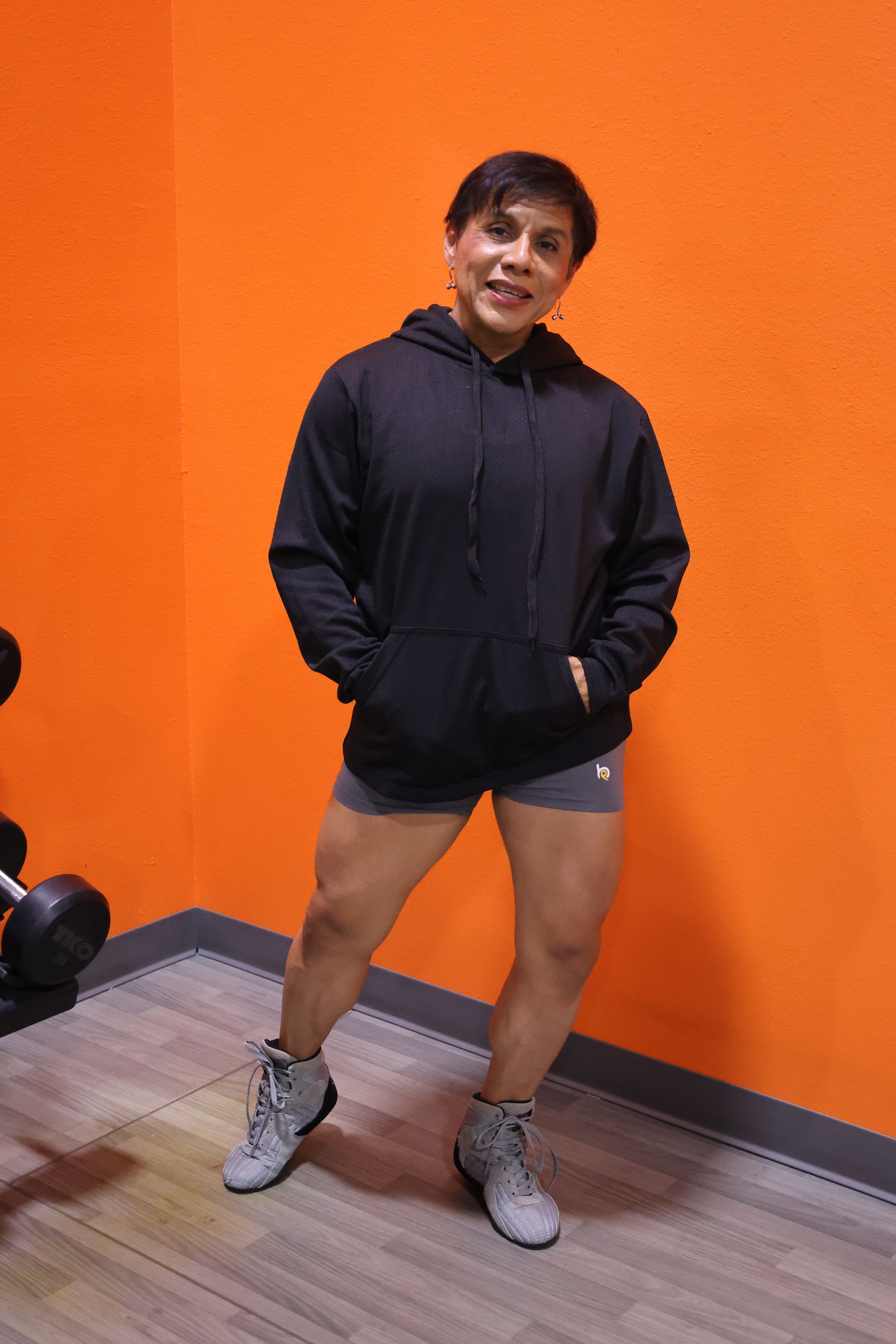 A woman in a black hoodie and shorts is standing in a gym.