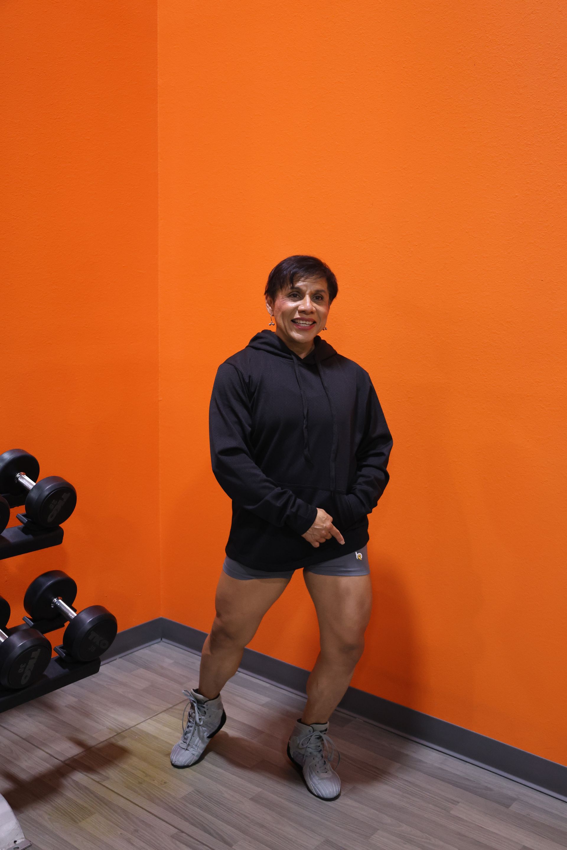 A woman is standing in a gym in front of an orange wall.