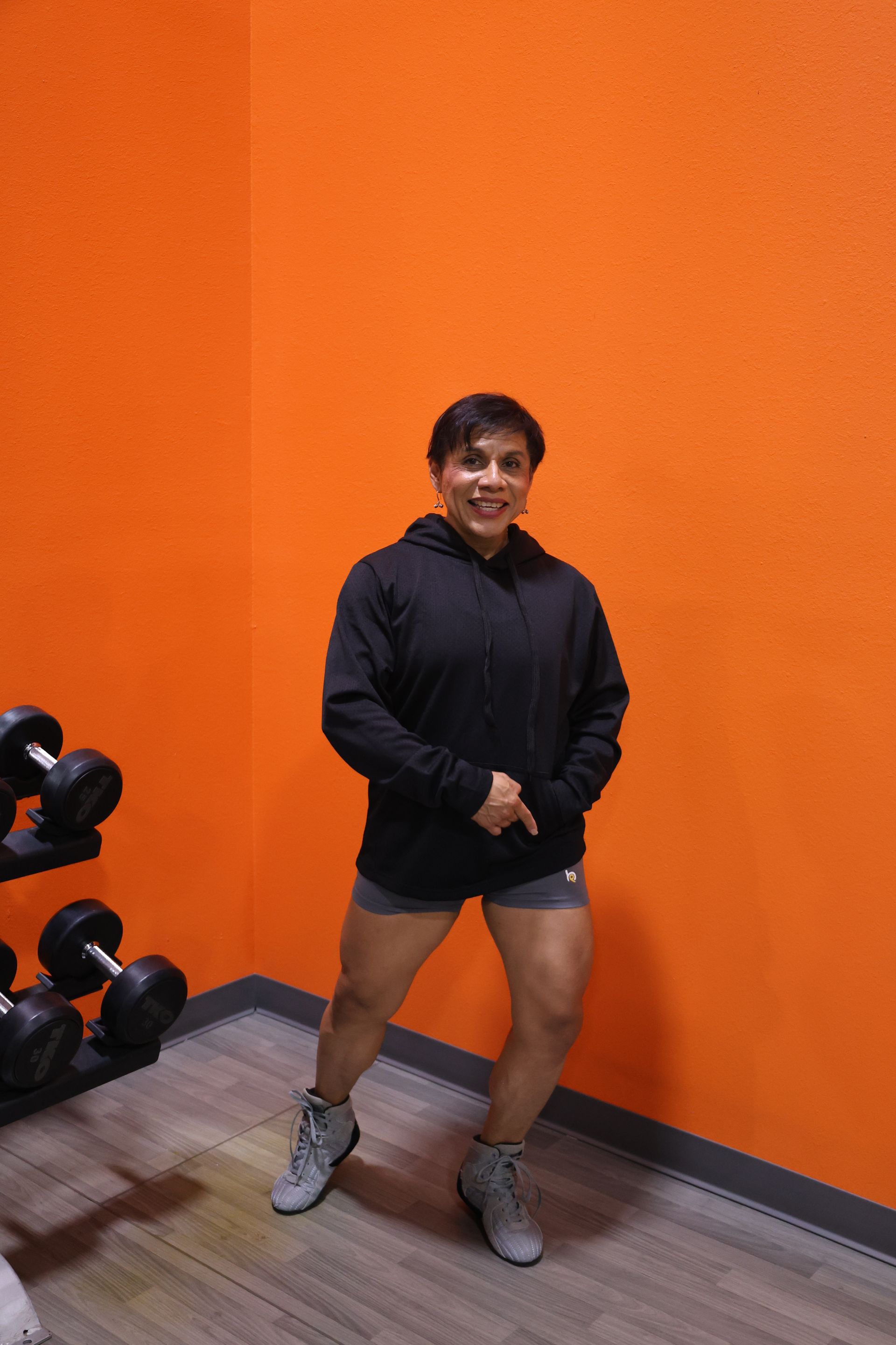 A woman is standing in a gym in front of an orange wall.