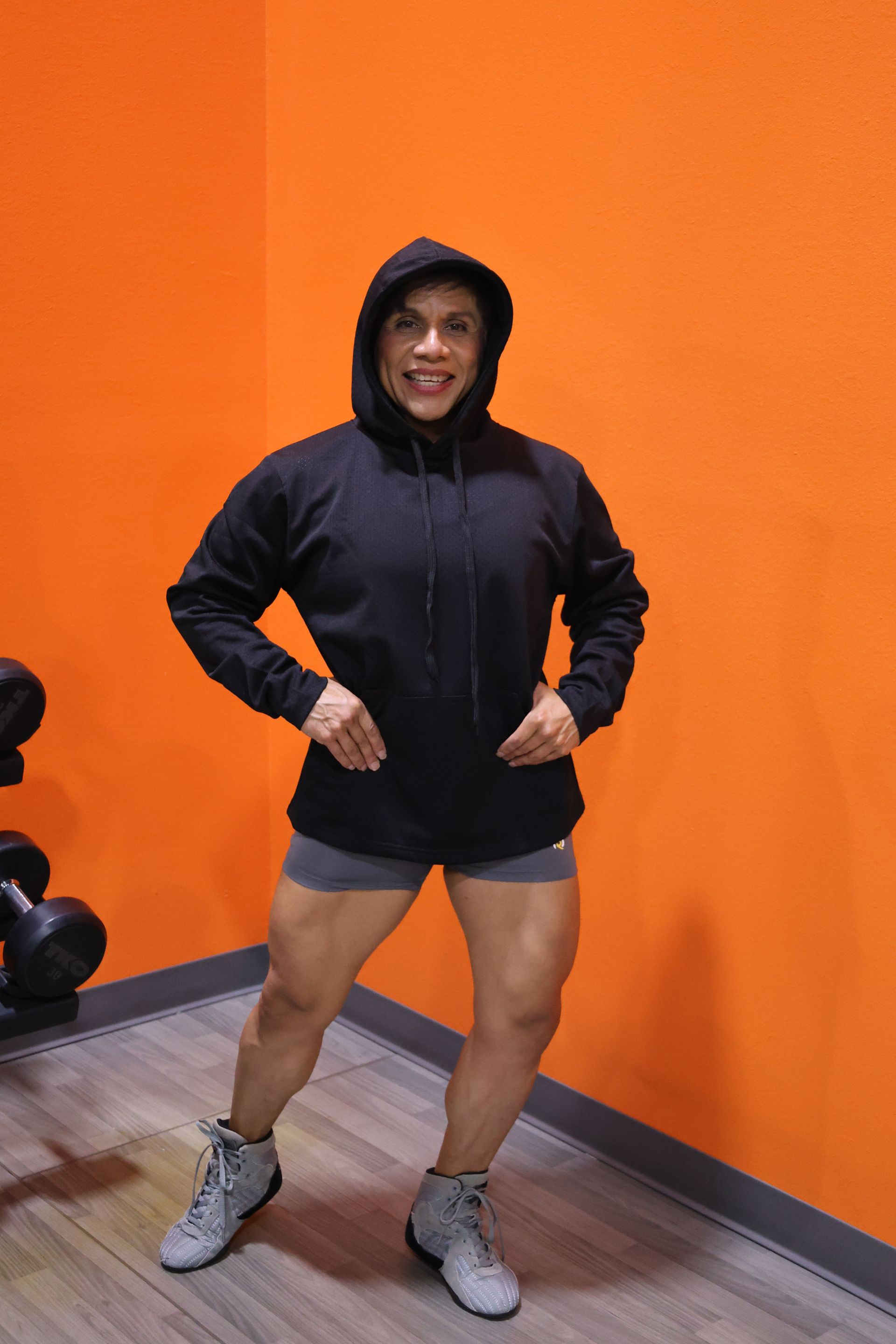 A woman wearing a black hoodie and shorts is standing in a gym.