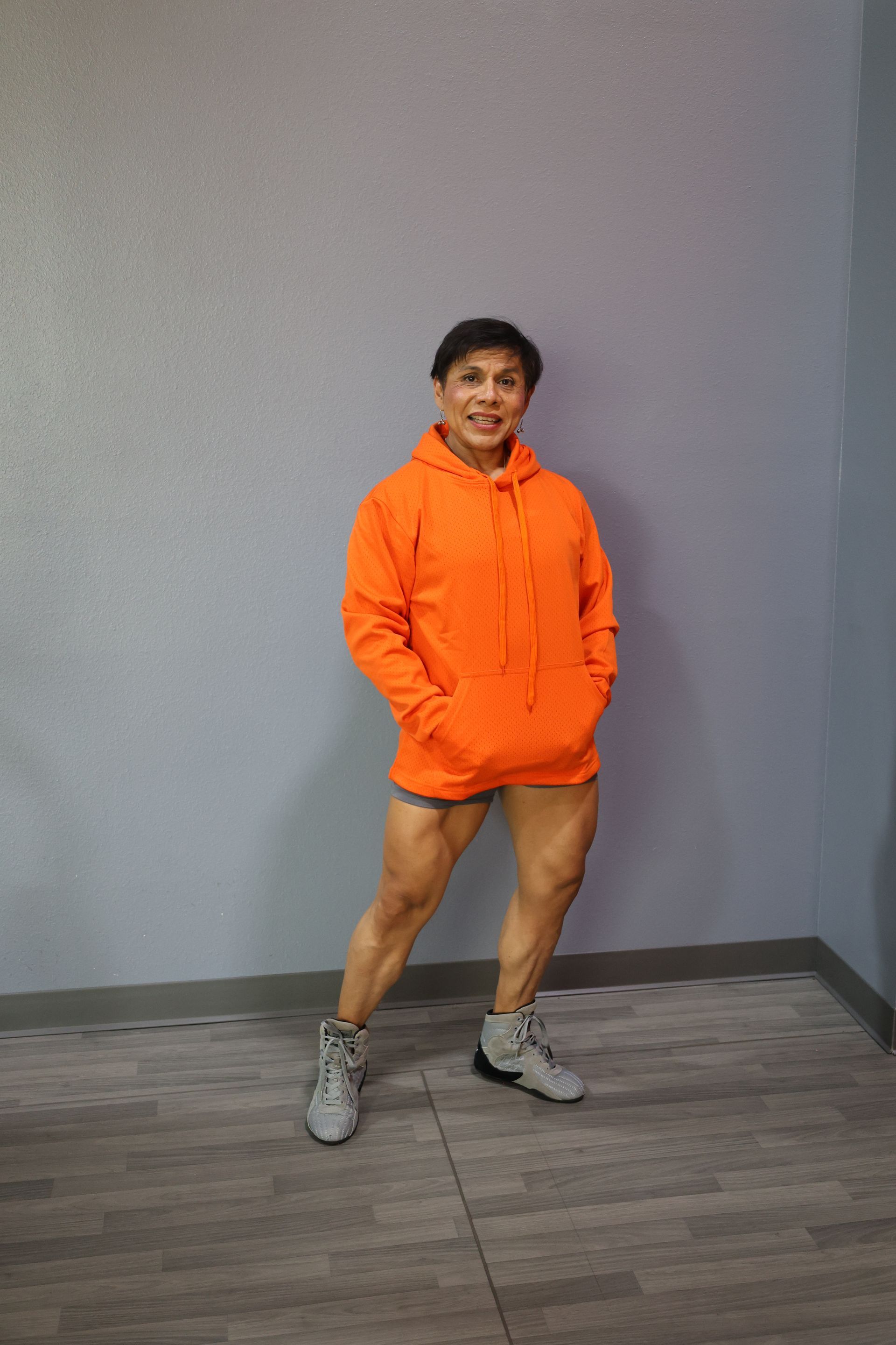 A man wearing an orange hoodie and shorts is standing in a room.