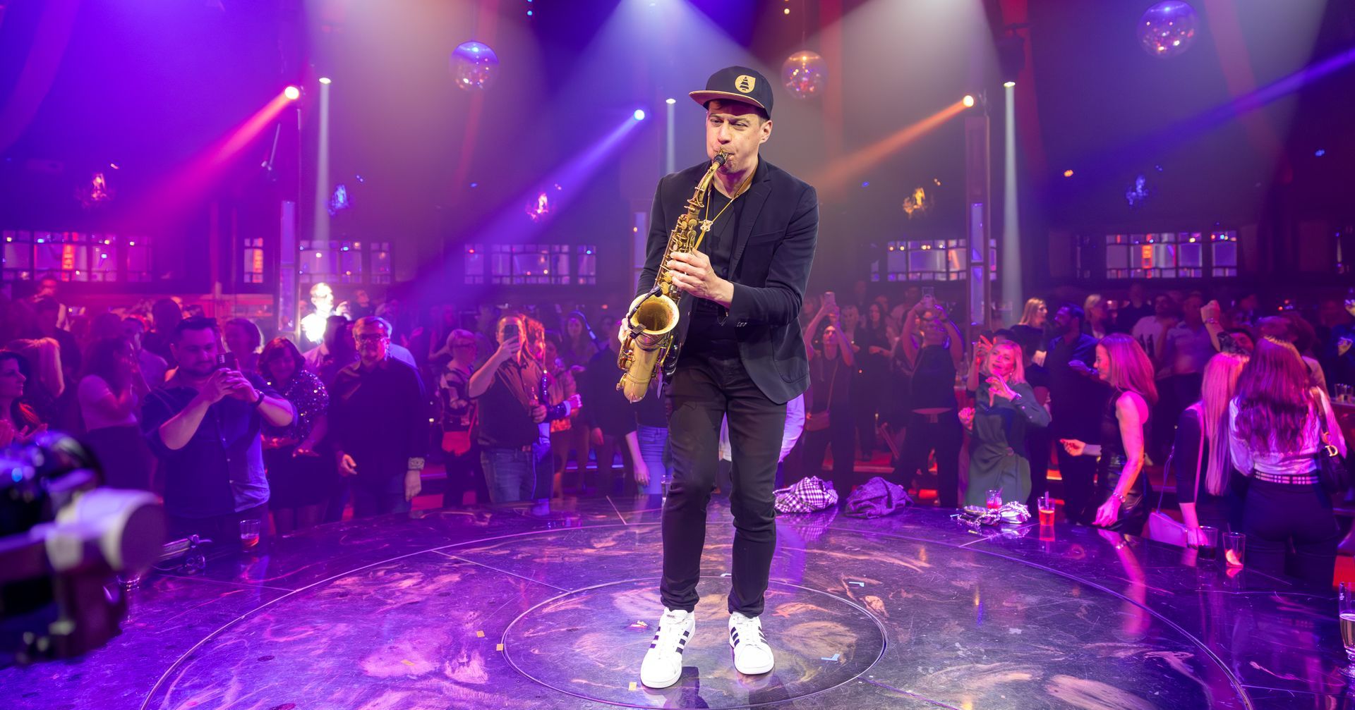 Ein Mann spielt auf einer Bühne vor einer Menschenmenge Saxophon.