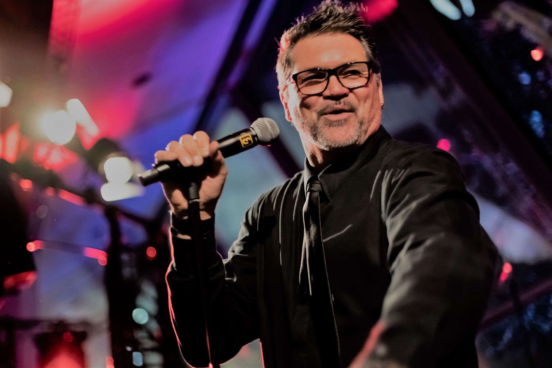 Ein Mann mit Brille singt auf einer Bühne in ein Mikrofon.
