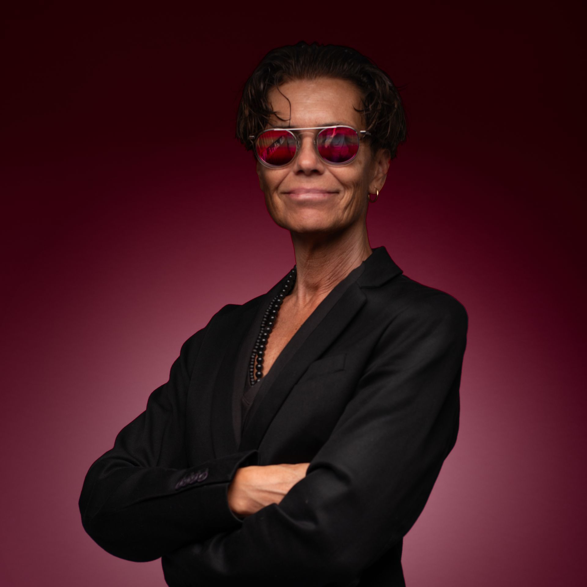 Eine Frau mit Sonnenbrille und schwarzer Jacke steht mit verschränkten Armen da.