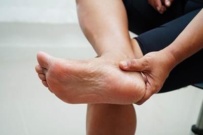 A woman is sitting on a chair holding her foot in pain.