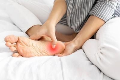A person is sitting on a bed holding their foot in pain.