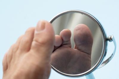 A person is looking at their foot in a mirror.