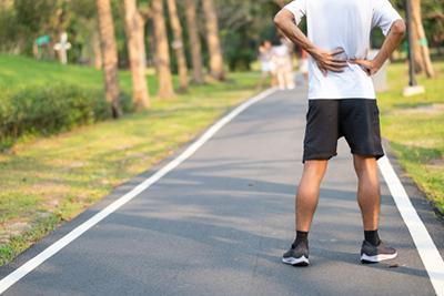A man is standing on a road holding his back in pain.
