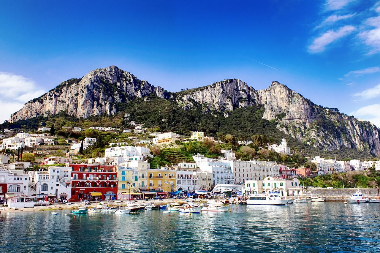 Vibrant Capri harbor with colorful buildings, boats, and the towering limestone cliffs under a bright blue sky