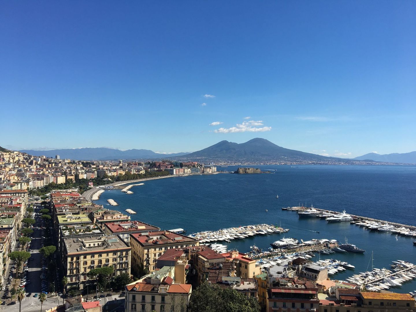 Scenic view of Mount Vesuvius overlooking the Bay of Naples, with a marina full of boats and the bustling cityscape.