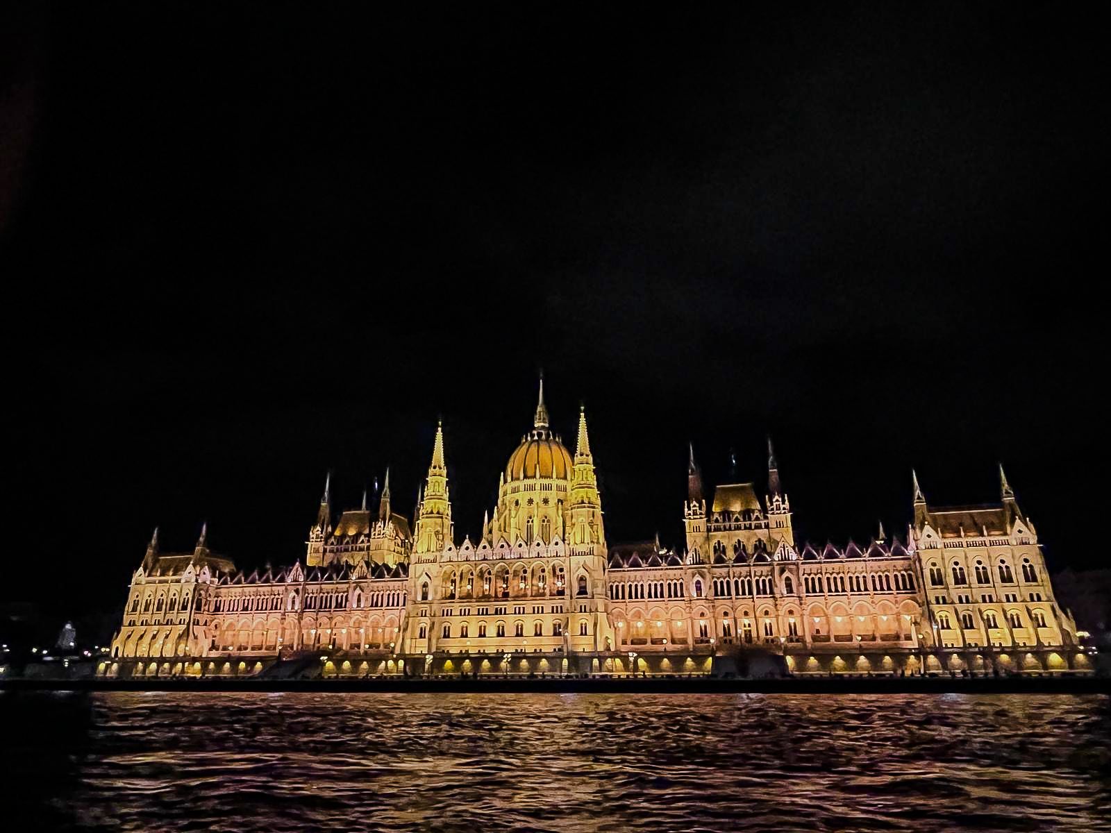 Hungarian Parliament Building illuminated at night, reflected in the water.