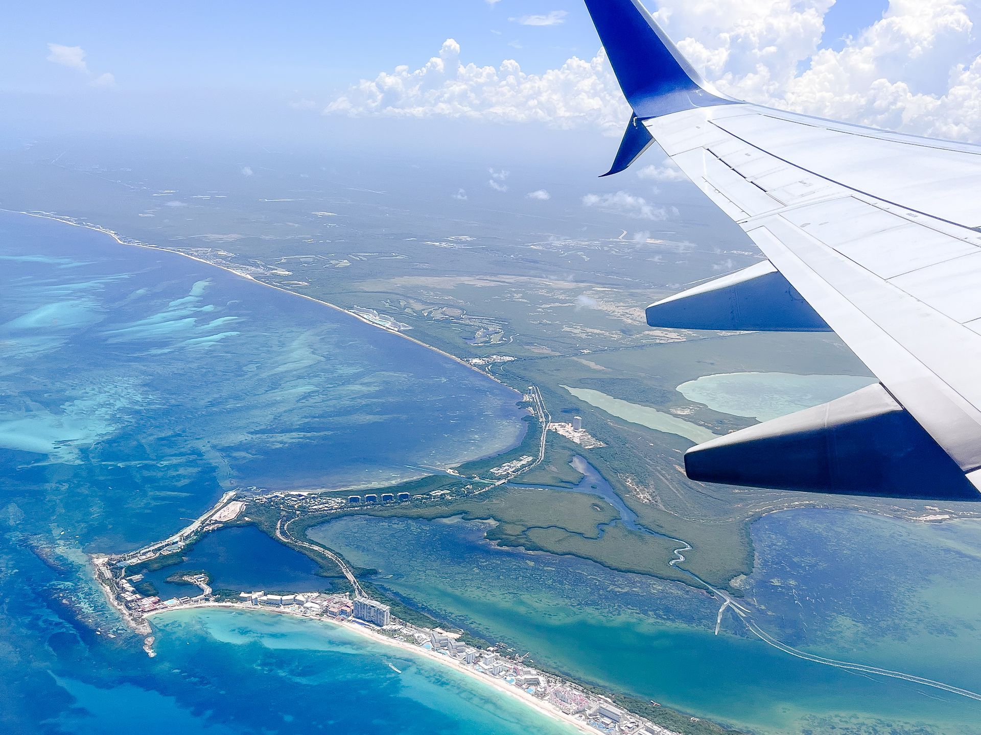 Airplane wing over a peninsula with turquoise water and white beaches.