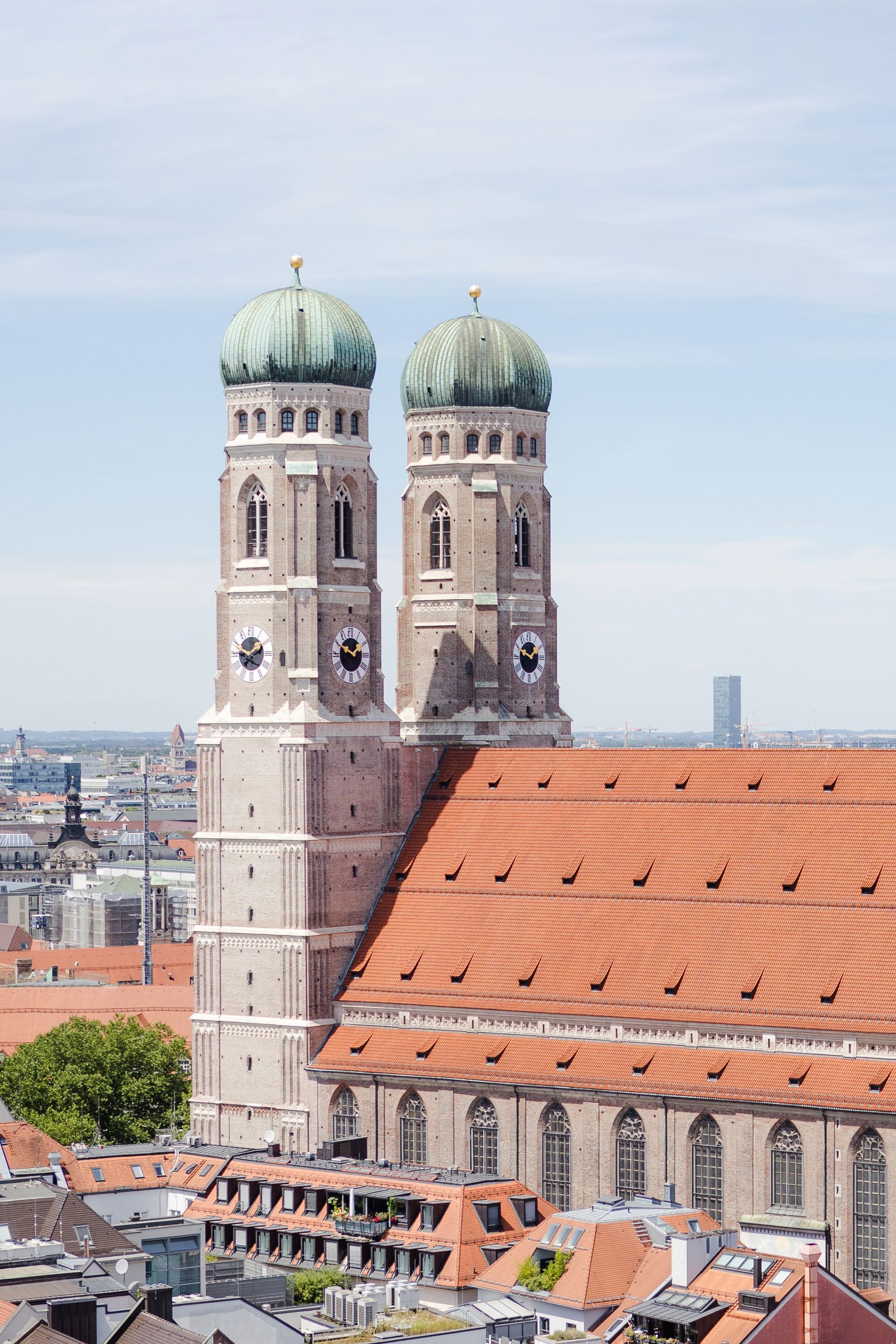 Frauenkirche in Munich, Germany, with two onion-domed towers, red tiled roof, and blue sky.