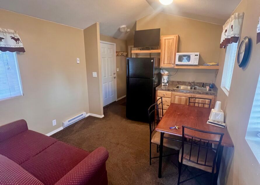 Small cabin interior with tan walls, brown carpet, and a kitchenette including a microwave, fridge, and sink.