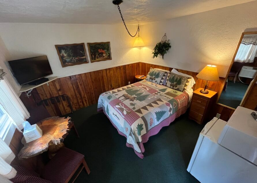 Cozy motel room with a double bed, small table, TV, and a full-length mirror.