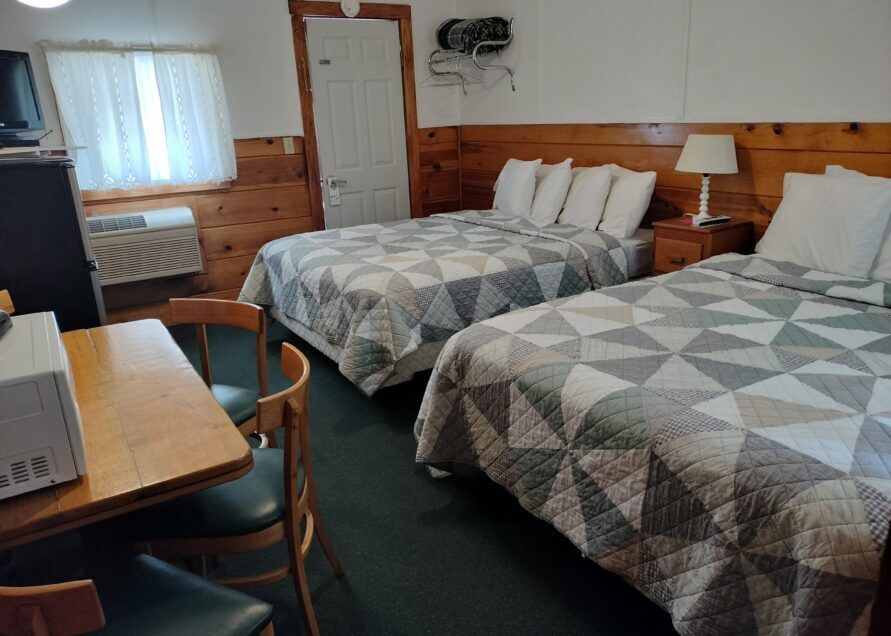 A small motel room with two double beds, a table with chairs, and a microwave.