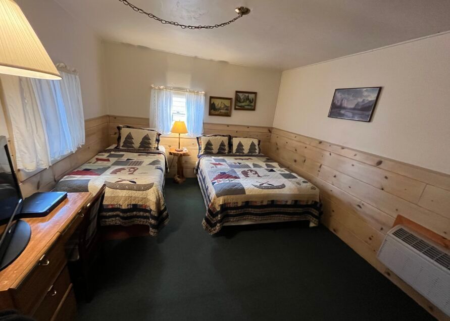 A cabin bedroom with two beds, a desk, and small windows.