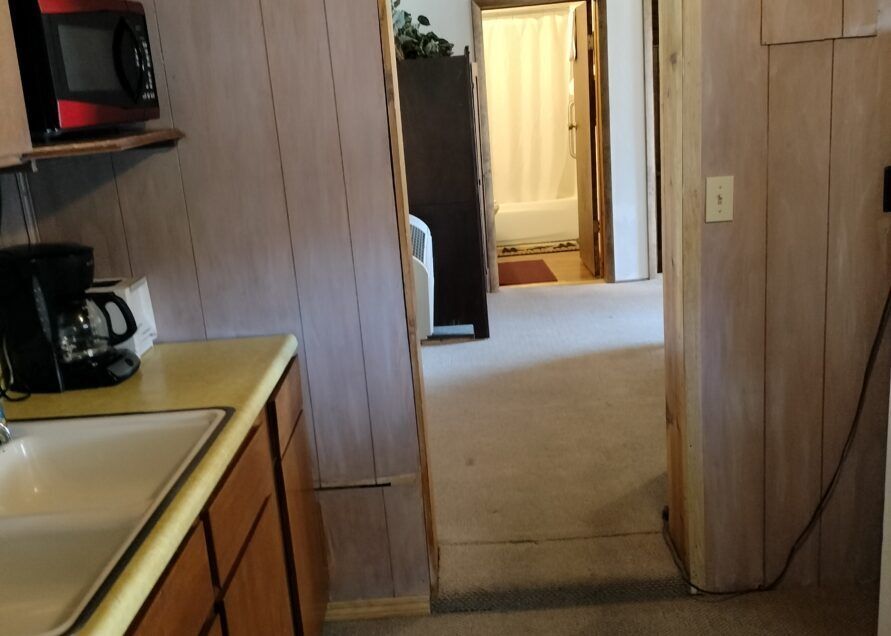 A kitchen and hallway. The kitchen features a microwave, coffee maker, and sink.