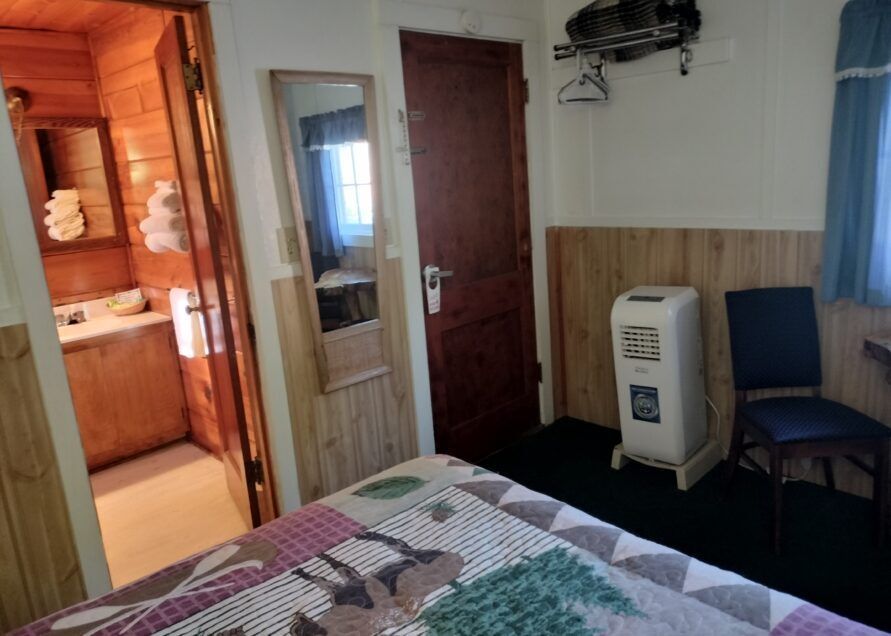 A small hotel room with wood paneling, a bed with a quilt, and a bathroom visible.