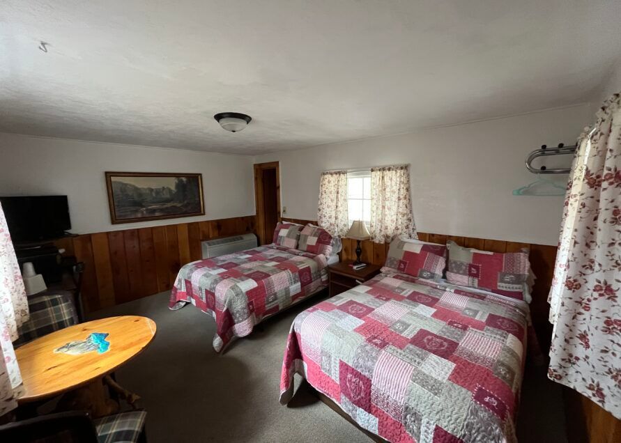 A motel room with two double beds, wood paneling, and floral patterned quilts and curtains.