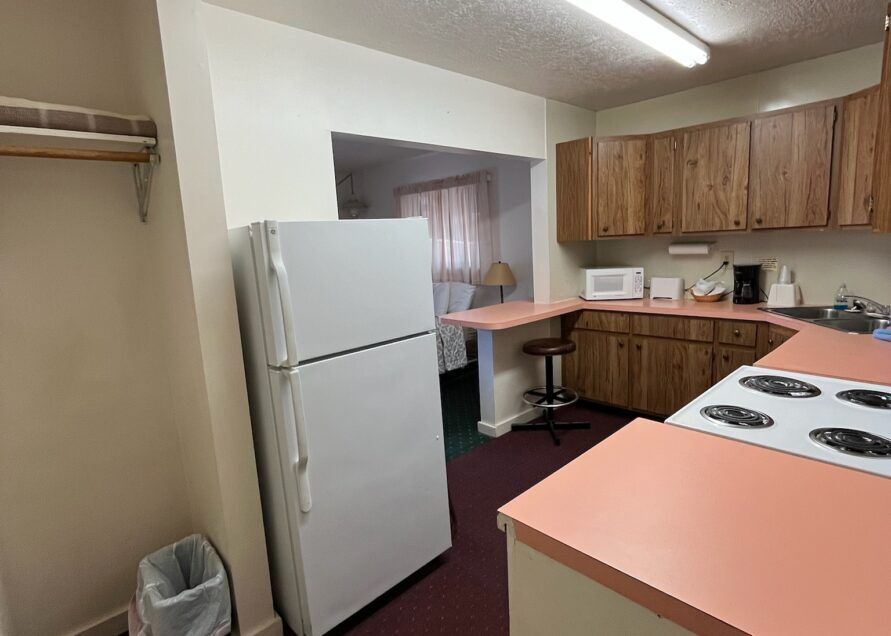 A small, dated kitchen with a white refrigerator, pink countertops, and wooden cabinets.