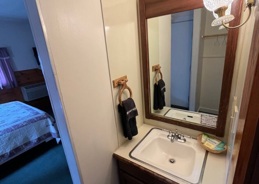 Bathroom with a sink, mirror, and towel rack, next to a bedroom with a bed.
