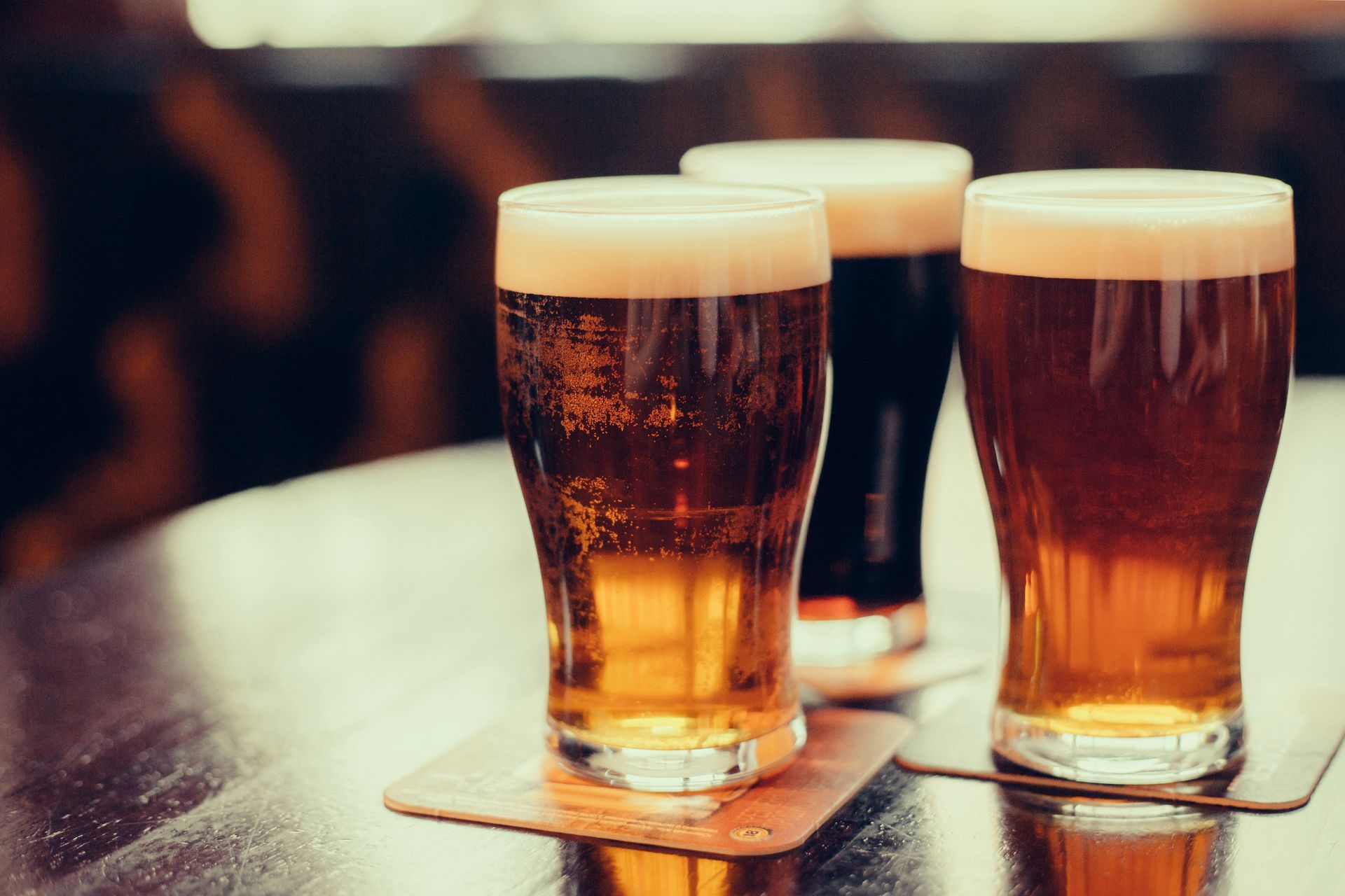 Three glasses of beer on a wooden table, showcasing varying amber hues and foamy heads.