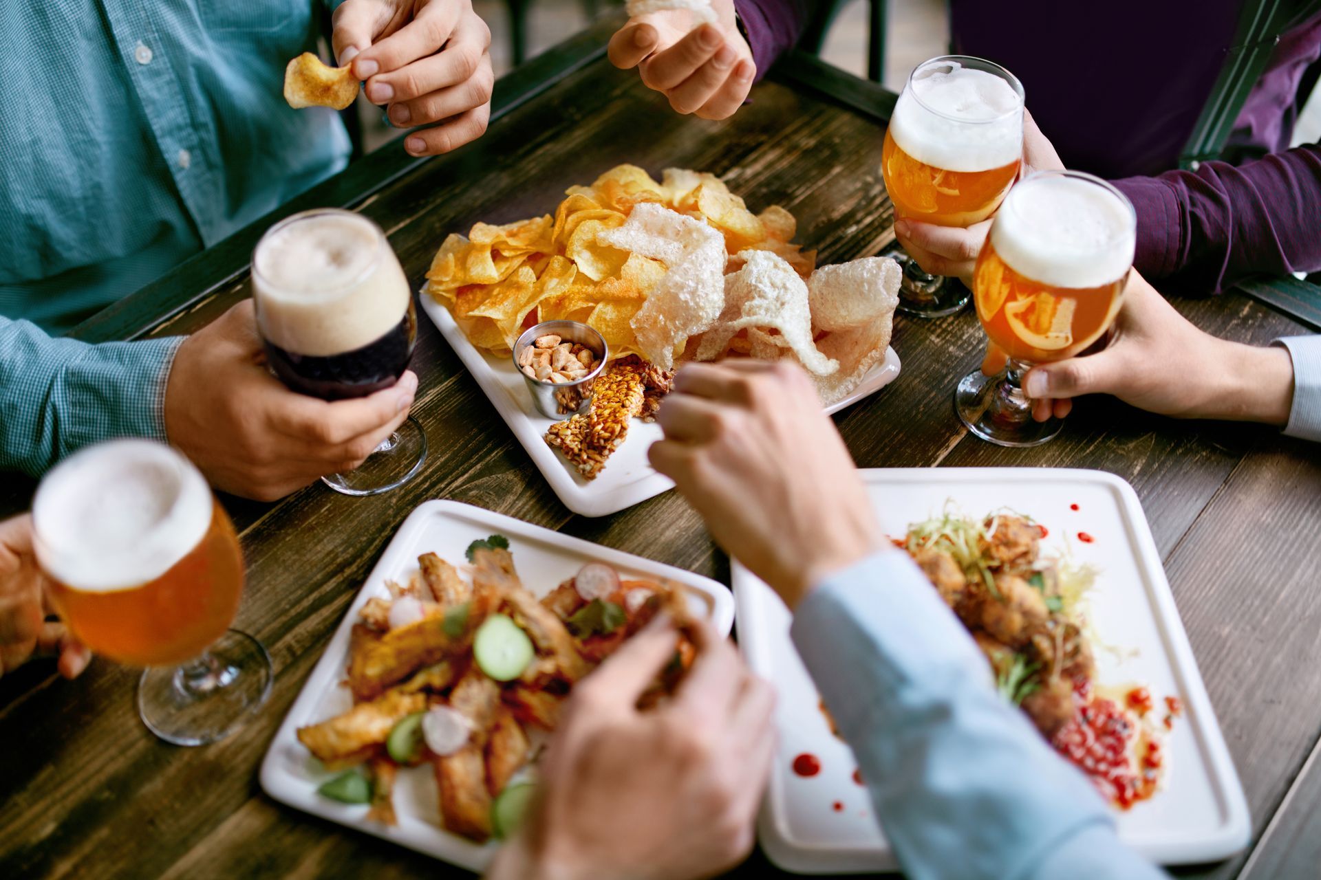 People at a table sharing beer and appetizers, including chips, fried foods, and dipping sauces.