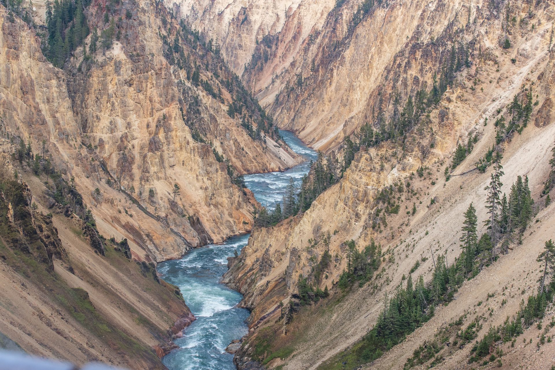 A deep canyon with a turquoise river winding through it; tan and green rocky walls rise on either side.