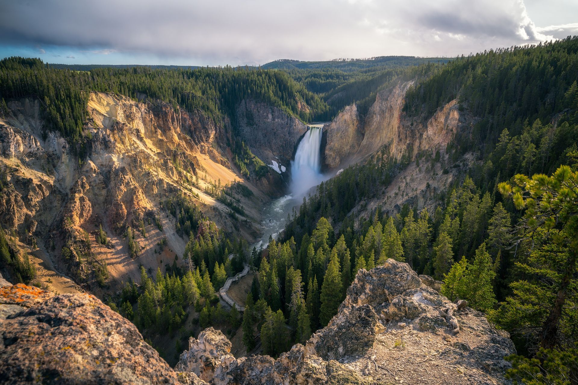 Grand Canyon of the Yellowstone with waterfall cascading into the canyon. Lush green trees line the canyon walls.