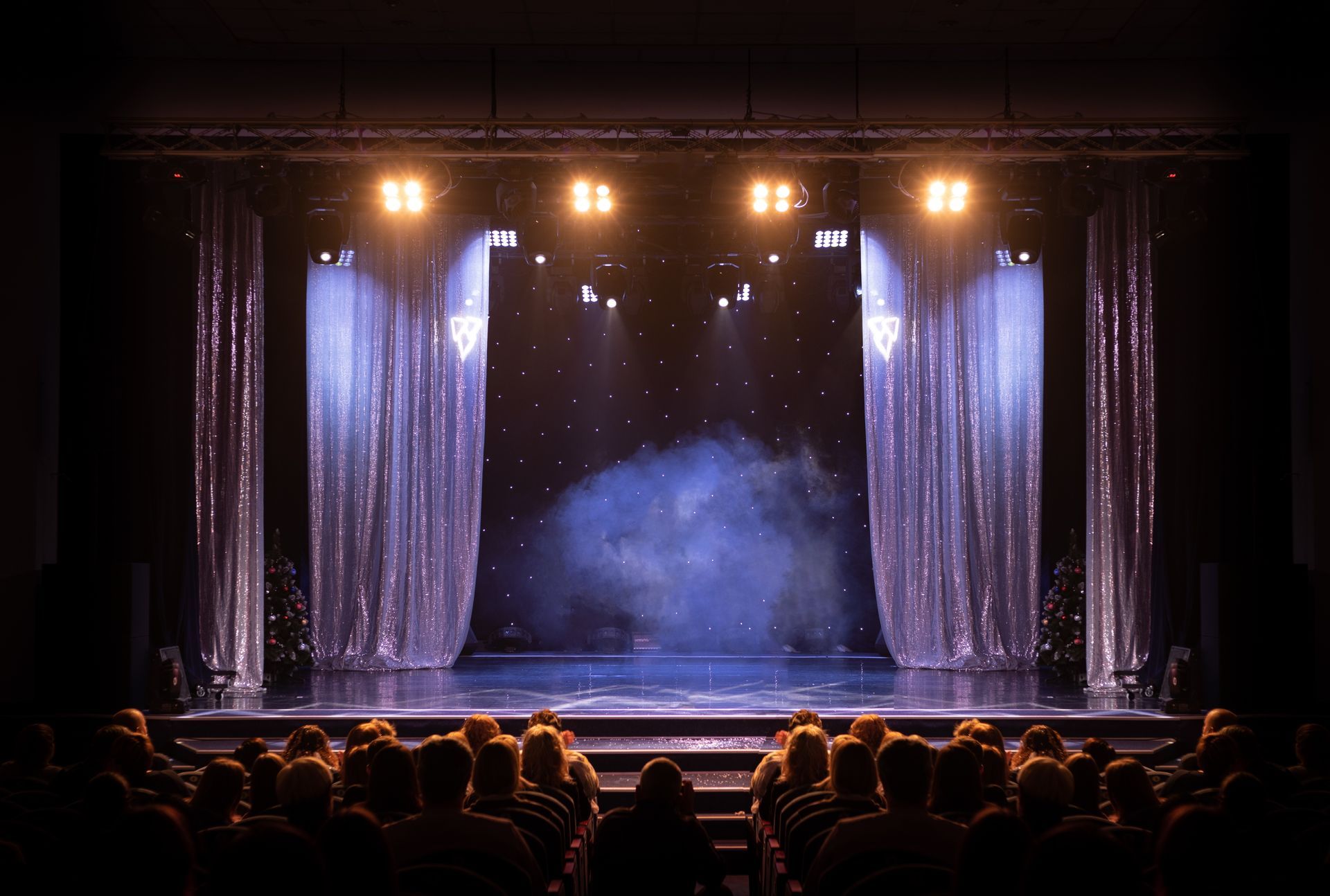 A brightly lit stage with curtains on either side, smoke, and an audience watching.