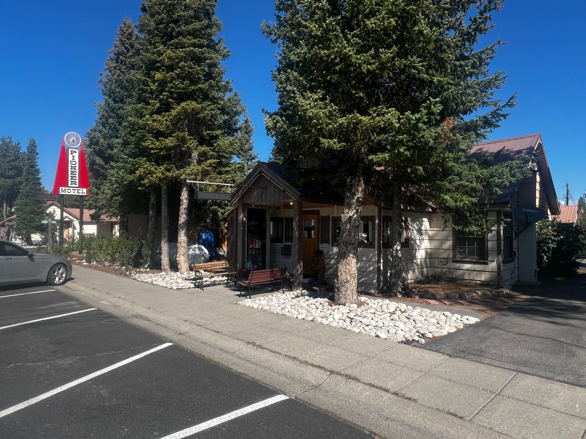 Small rustic shop with trees out front, stone facade, and a sign on the left.