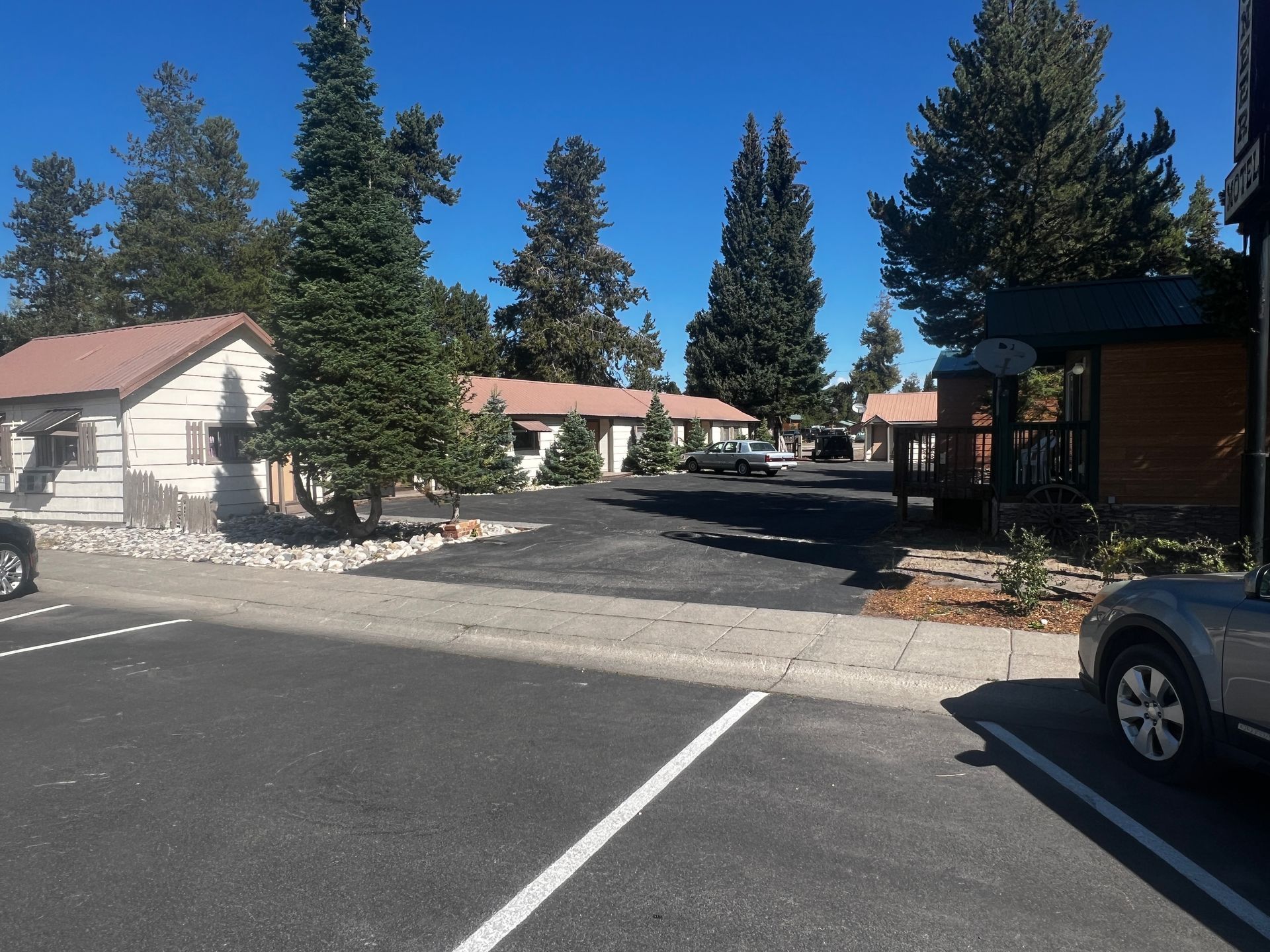Parking lot in front of small, one-story buildings with trees under a blue sky.