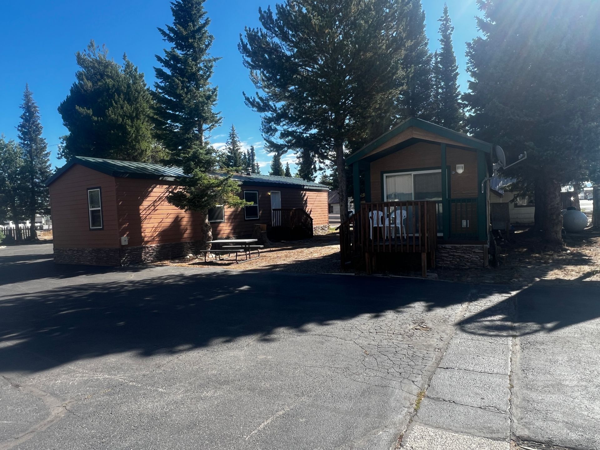 Cabins in a campground, brown exteriors, surrounded by trees, sunny day.