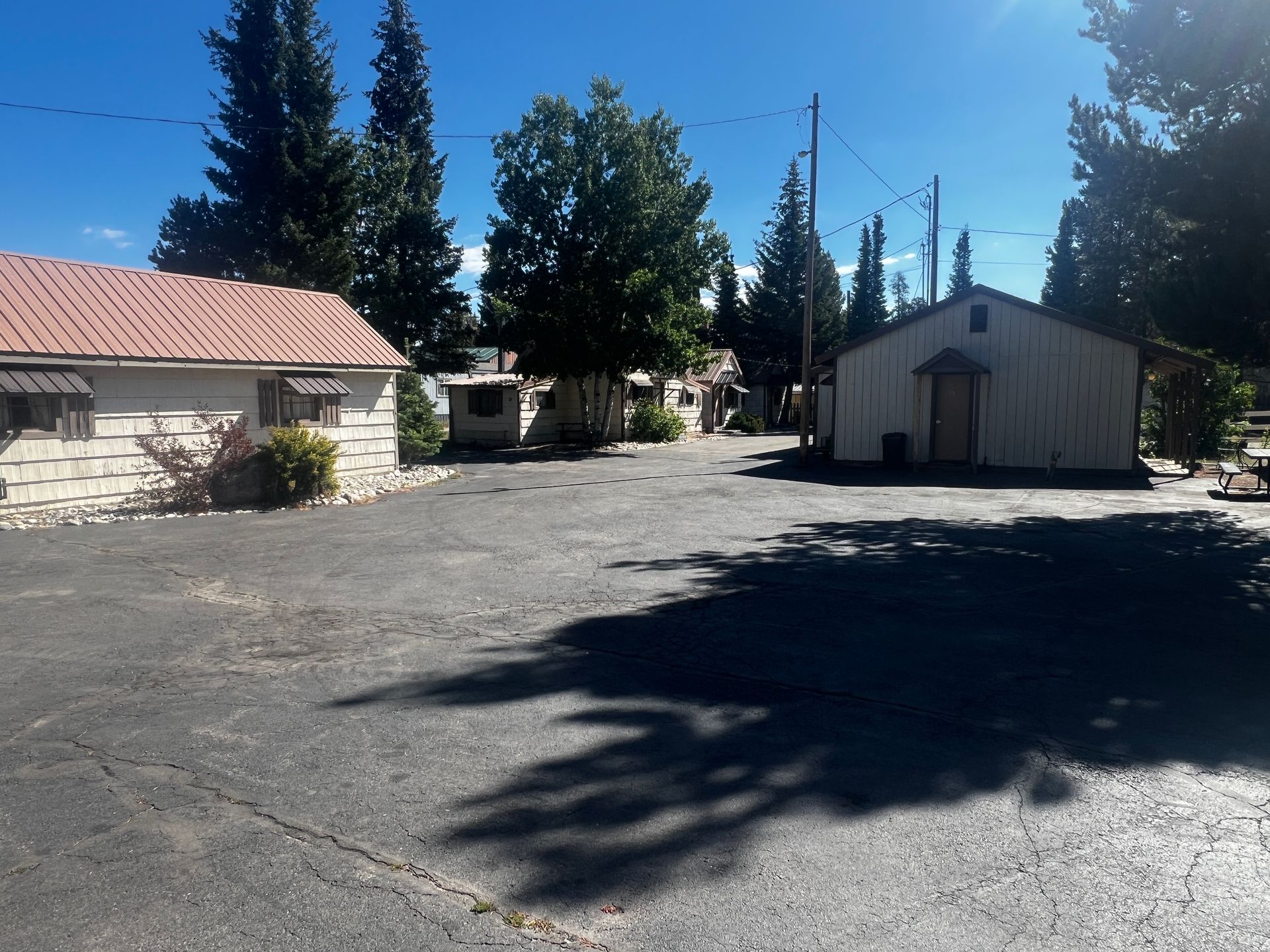A sunny shot of a parking lot with old, white buildings and trees under a blue sky.