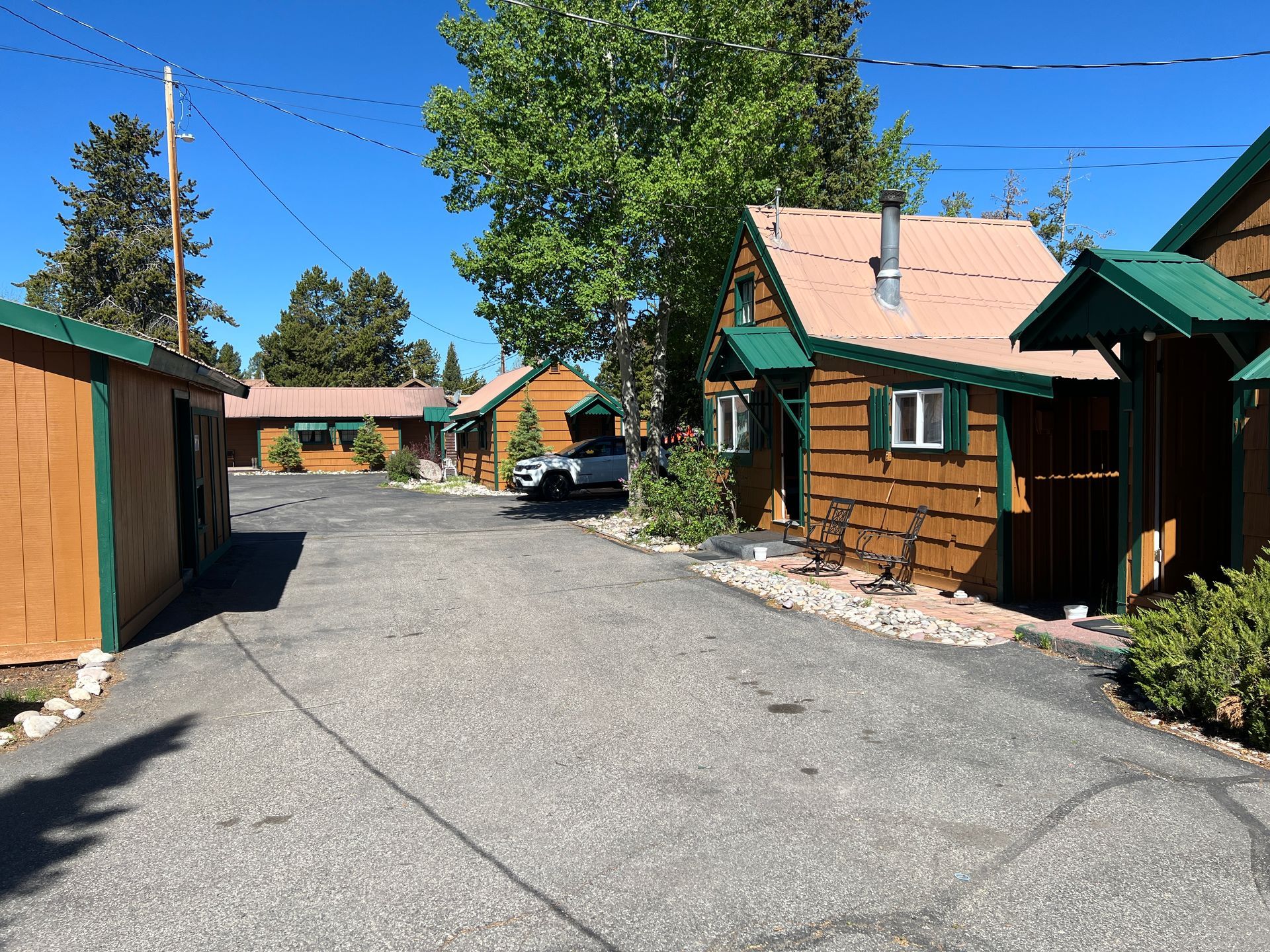 Cabins along a gravel road under a bright blue sky, with a parked car in the center.