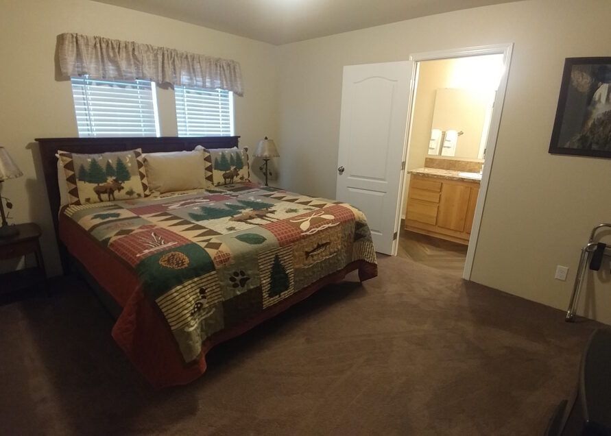 Bedroom with a queen-sized bed, patterned quilt, and an attached bathroom. The room has brown carpet and beige walls.